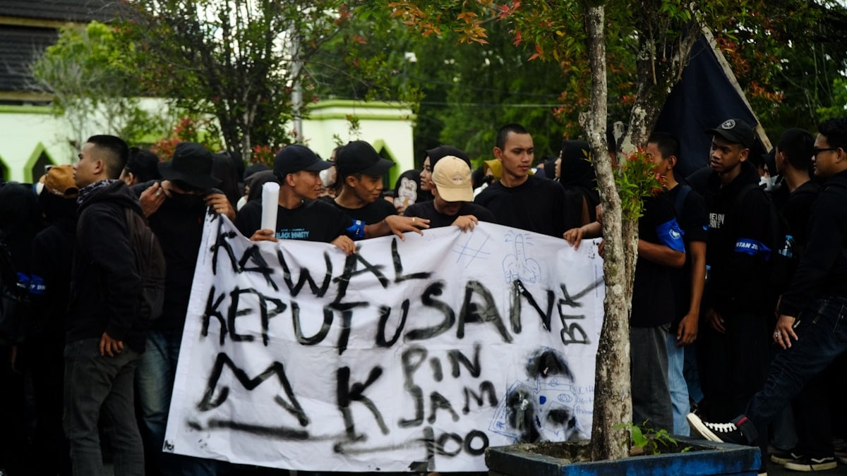 A group of people standing around a tree holding a sign